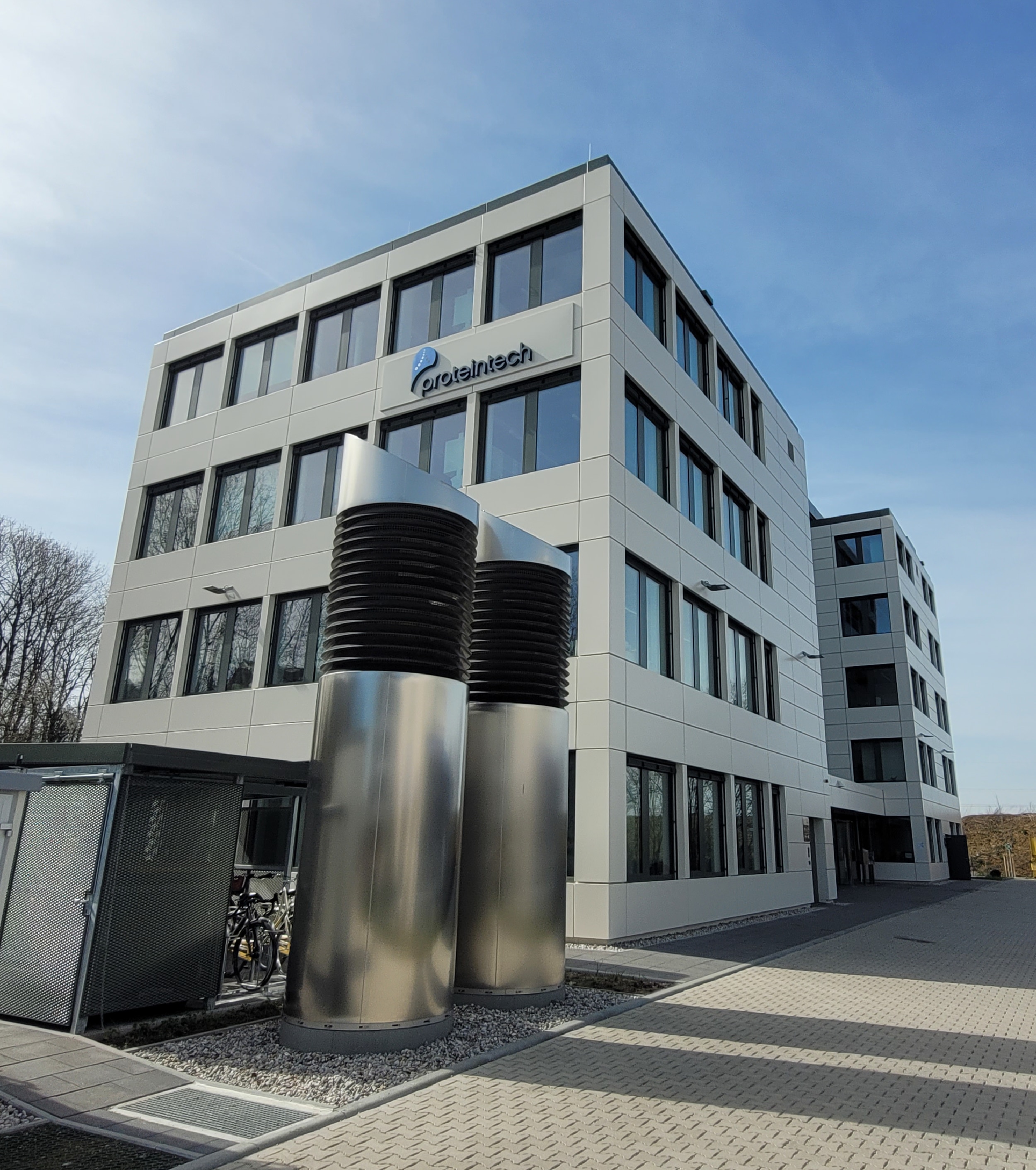Photo of a modern office or lab building exterior with large windows and metal ventilation stacks in the foreground